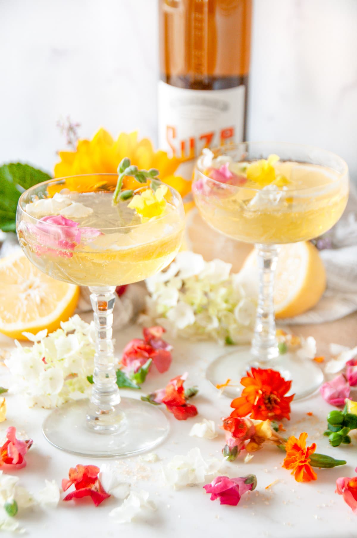 Sparkling Suze Wildflower Cocktail in crystal glasses with edible flowers on white marble
