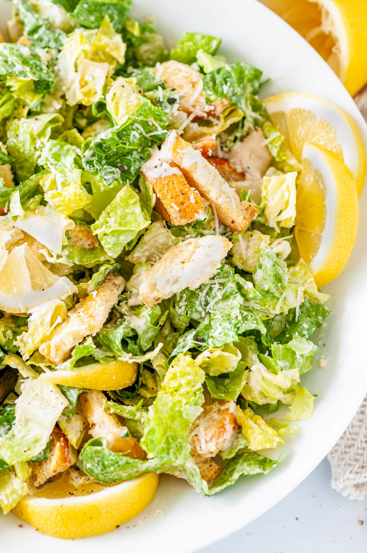 Vegetarian Caesar Salad Dressing tossed with romaine lettuce, lemons and croutons in white bowl close up