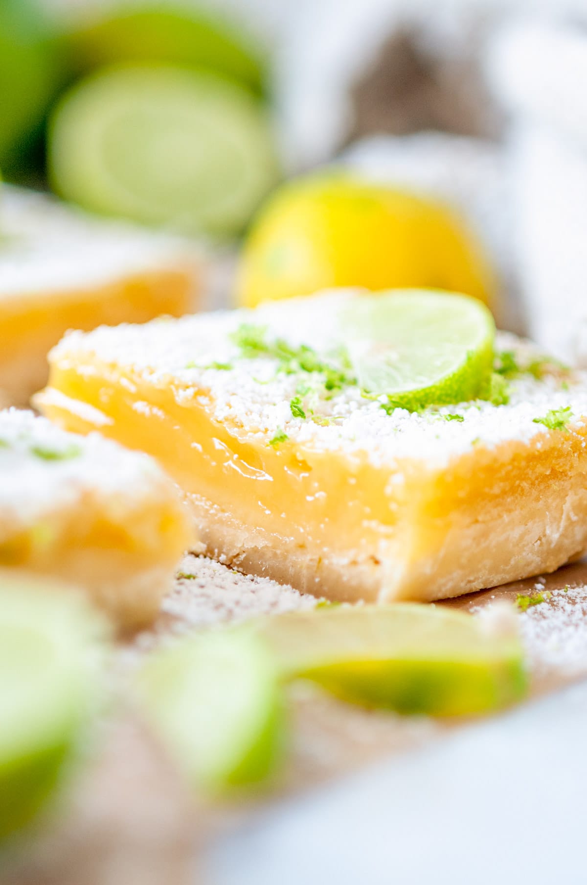 Easy Zesty Lime Bars with powdered sugar and key lime slices on brown parchment and white marble