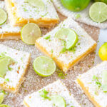 Easy Zesty Lime Bars with powdered sugar and key lime slices on brown parchment and white marble
