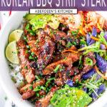 Korean BBQ Strip Steak in white bowl with rice, avocado, cabbage mix, kimchi and limes topped with green onion, chives, and sesame seeds on white marble - purple rectangle overlay with white text