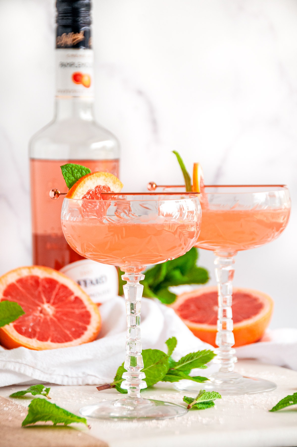 Pink Pamplemousse Gin Cocktail in crystal glasses with fresh mint and Giffard liqueur bottle on white marble