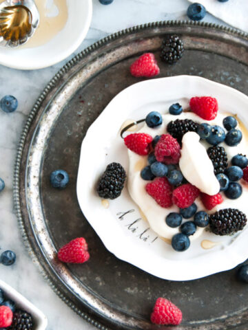summer berries with limoncello whipped cream on white plate and gray marble with honey spoon