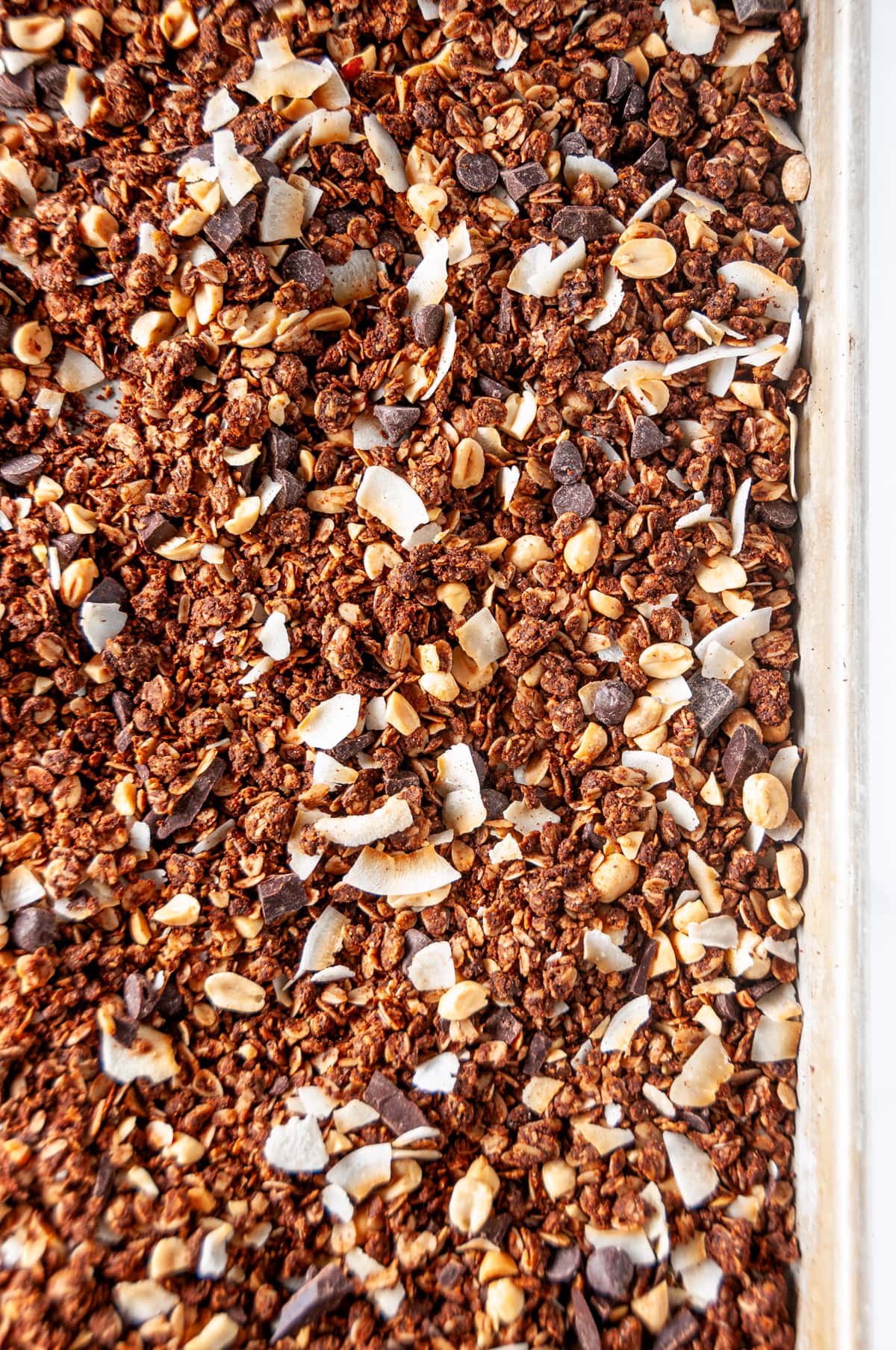 Chocolate peanut butter granola baked on silver baking sheet on white marble overhead view