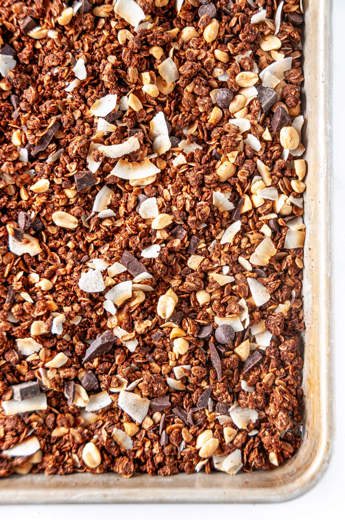 Chocolate peanut butter granola baked on silver baking sheet on white marble overhead view close up