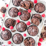 Chocolate Raspberry Veggie Muffins in silver muffin tray on white marble with chocolate chips overhead view