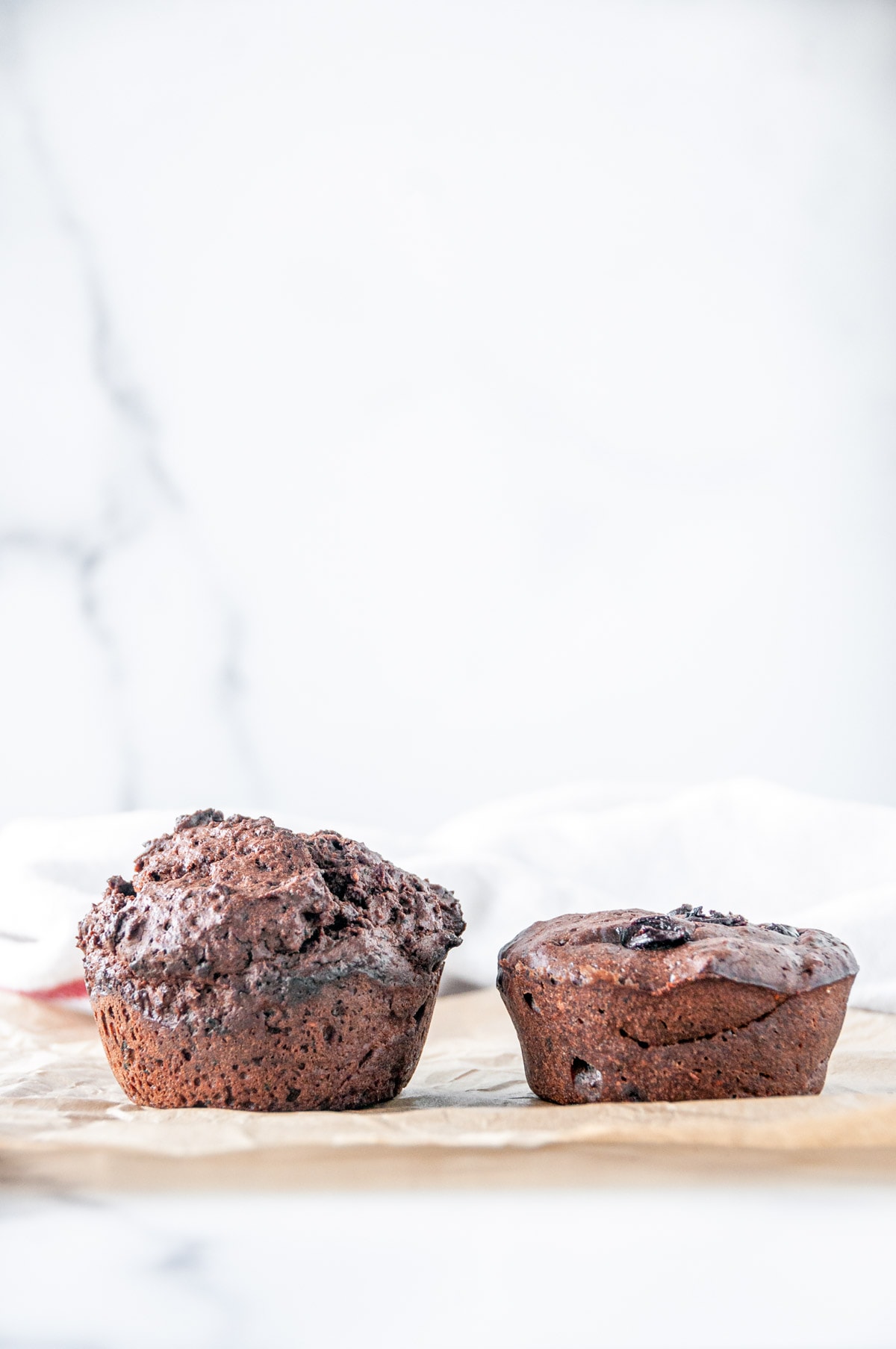 Chocolate raspberry veggie muffins pair one very tall and fluffy one like a hockey puck on white marble