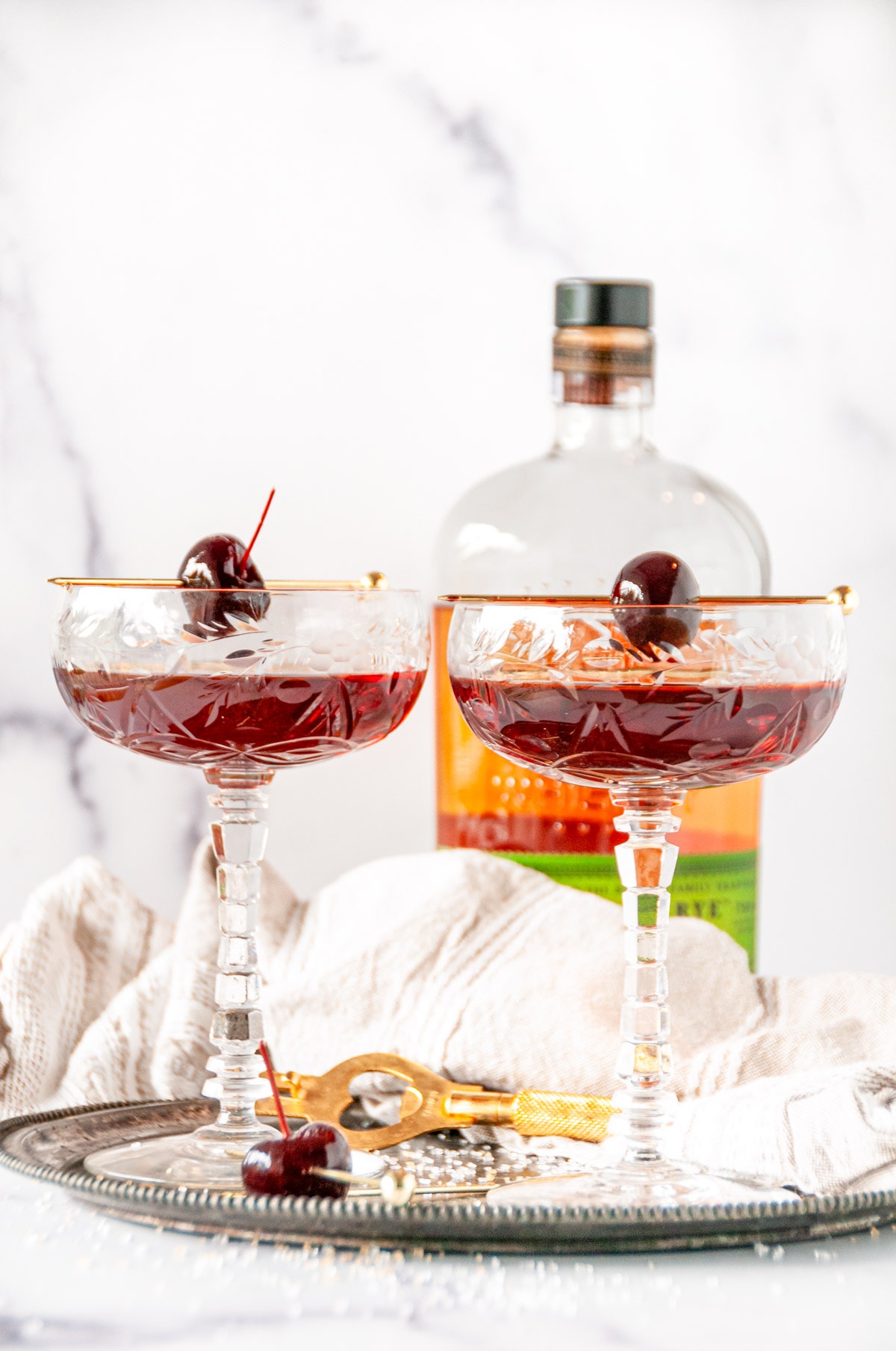 Classic Manhattan Cocktail in coupe glasses with maraschino cherries on gray plate with rye whiskey in background