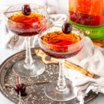 Classic Manhattan Cocktail in coupe glasses with maraschino cherries on gray plate with rye whiskey in background