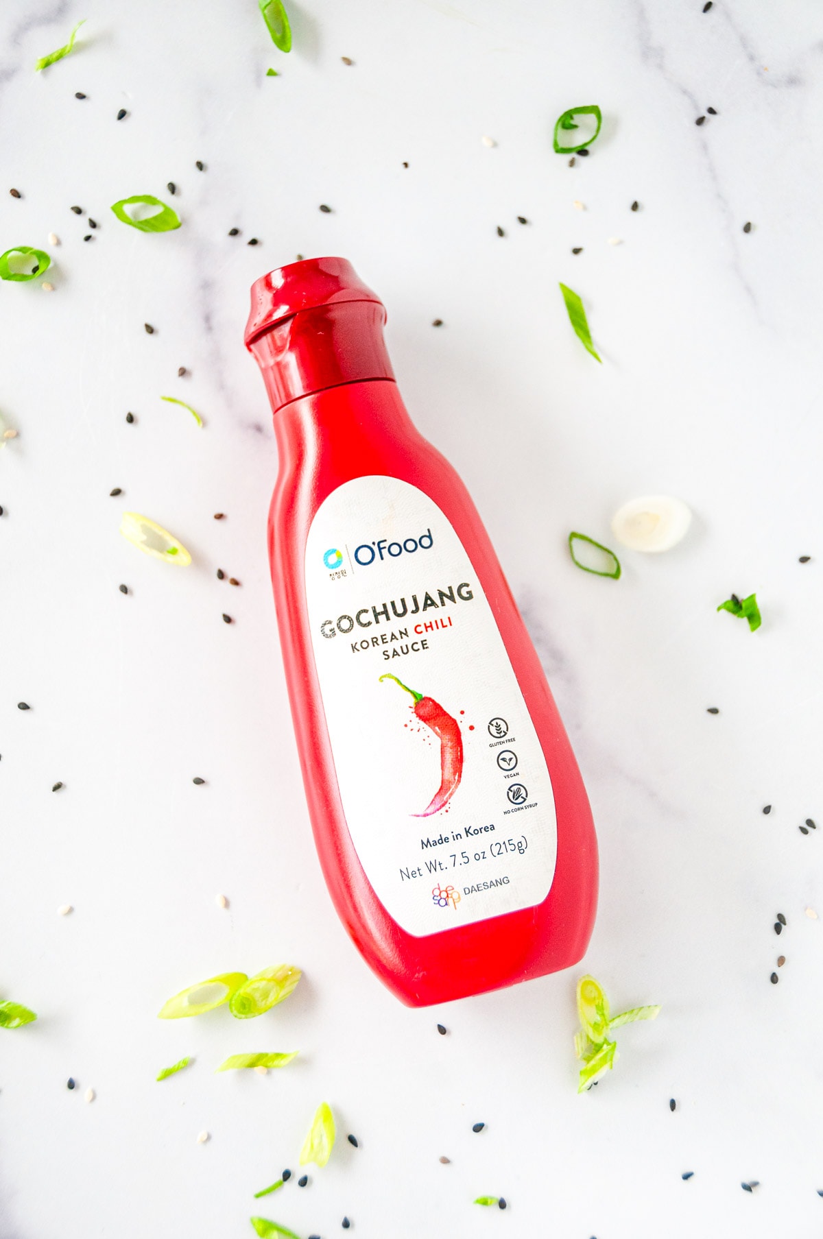 gochujang sauce bottle on white marble with green onion and sesame seeds