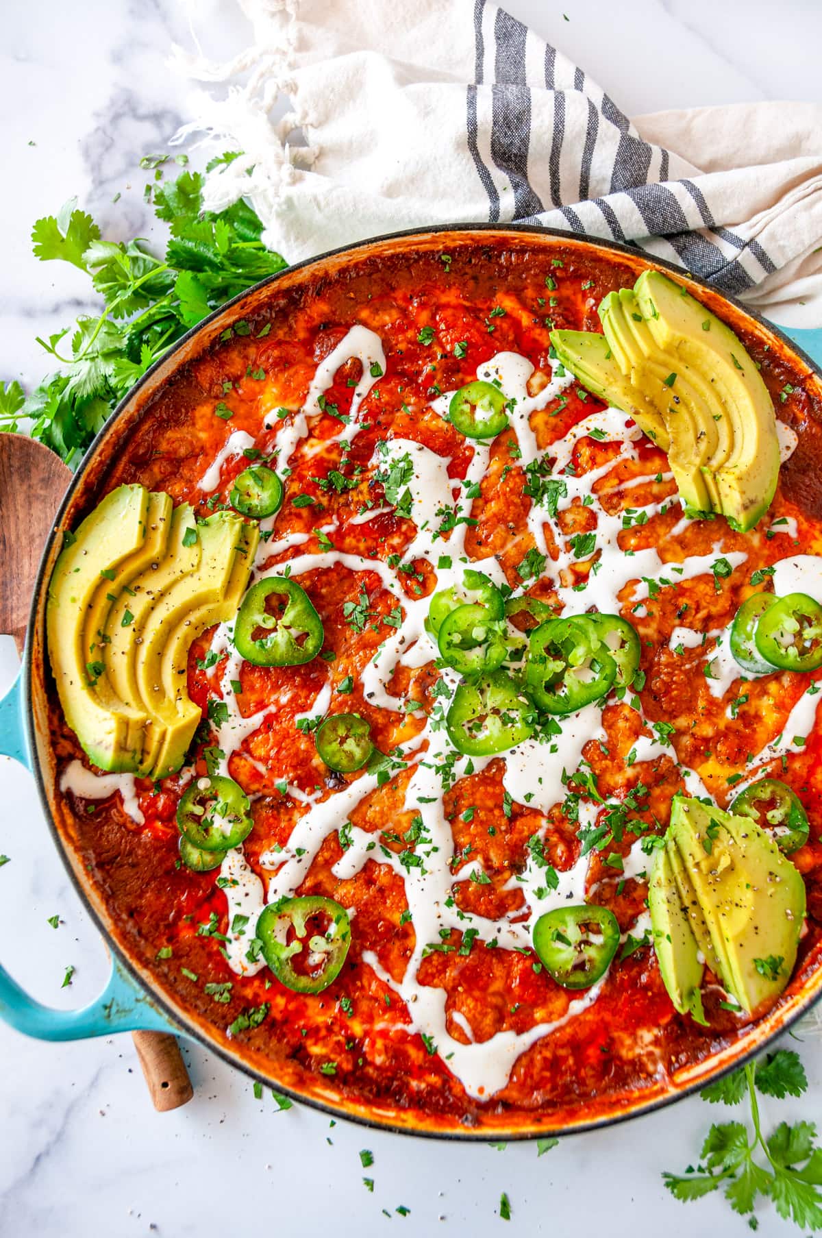 One Pot Red Enchilada Bake with sliced avocado, jalapeno, cilantro, and crema Mexicana drizzled on top