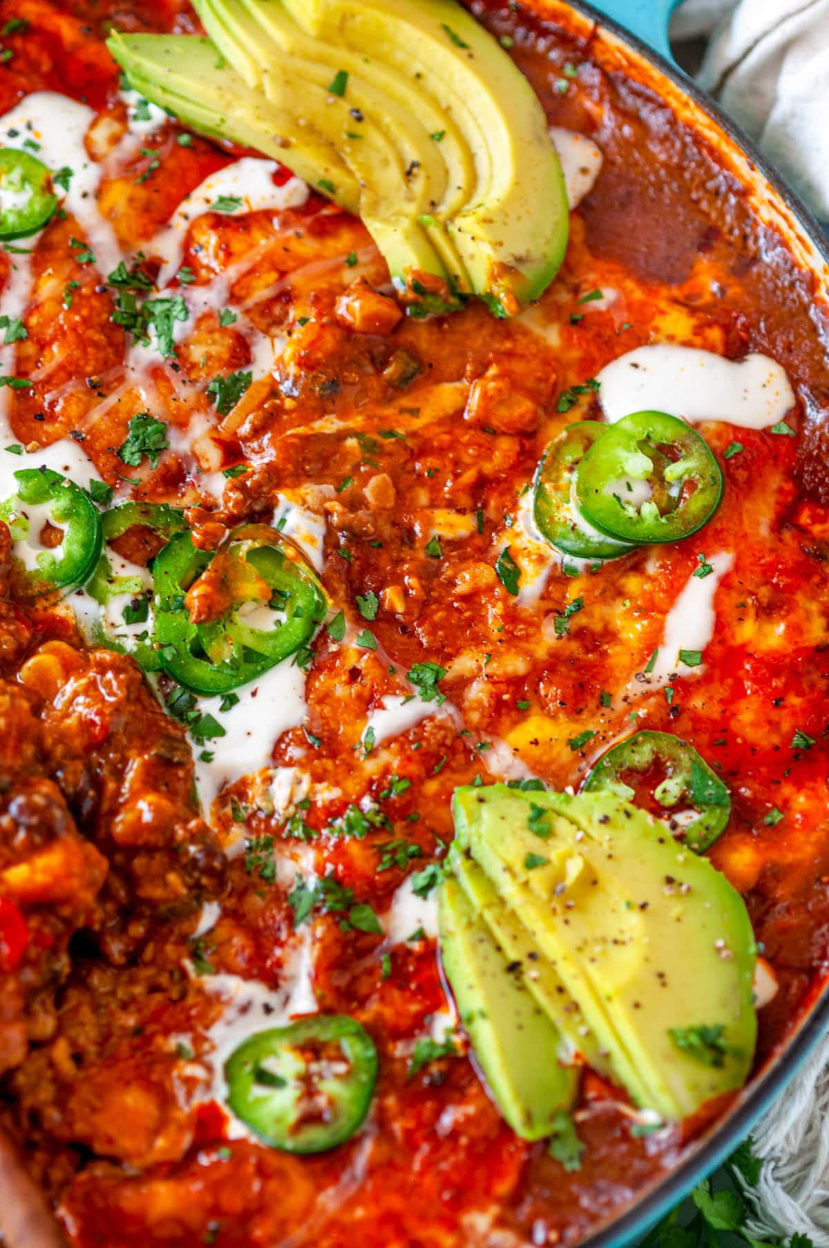 One Pot Red Enchilada Bake with sliced avocado, jalapeno, cilantro, and crema Mexicana drizzled on top