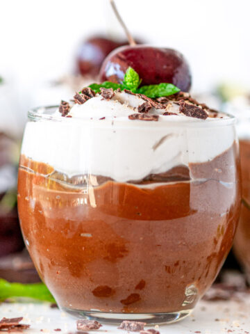 Avocado Chocolate Mousse in small dessert glasses with chocolate, mint, and cherries on white marble close up