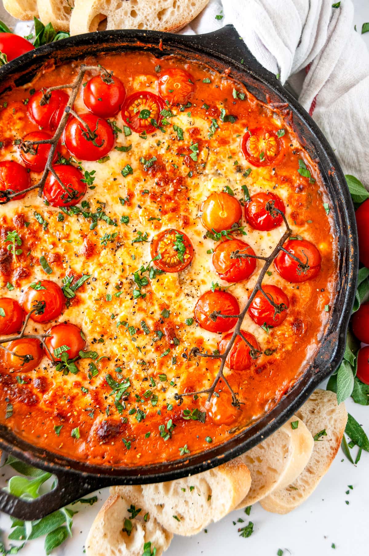 Cheesy White Bean Skillet Bake with sliced baguette and cherry tomatoes in lodge cast iron skillet on white marble
