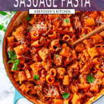 Creamy spicy sausage pasta in blue le creuset braiser with wooden spoon and fresh basil garnish on white marble overhead view - purple rectangle with white text overlay