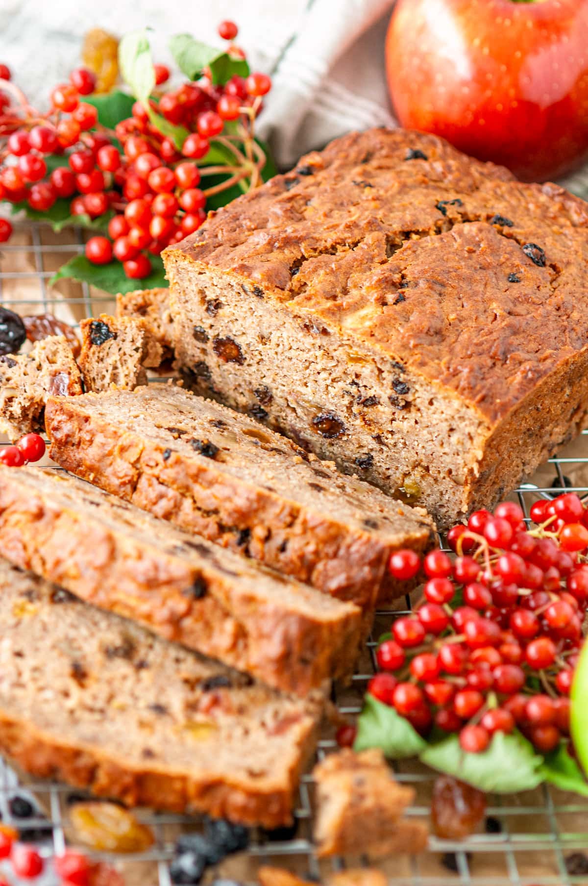 Spiced Currant Apple Bread sliced on wire rack and white marble sprinkled with raisins and surrounded with fresh currants