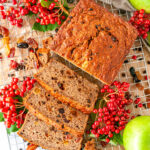 Spiced Currant Apple Bread sliced on wire rack and white marble sprinkled with raisins and surrounded with fresh currants