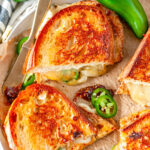 Spicy Grilled Cheese Sandwich sliced into halves with fresh jalapeno peppers on parchment paper
