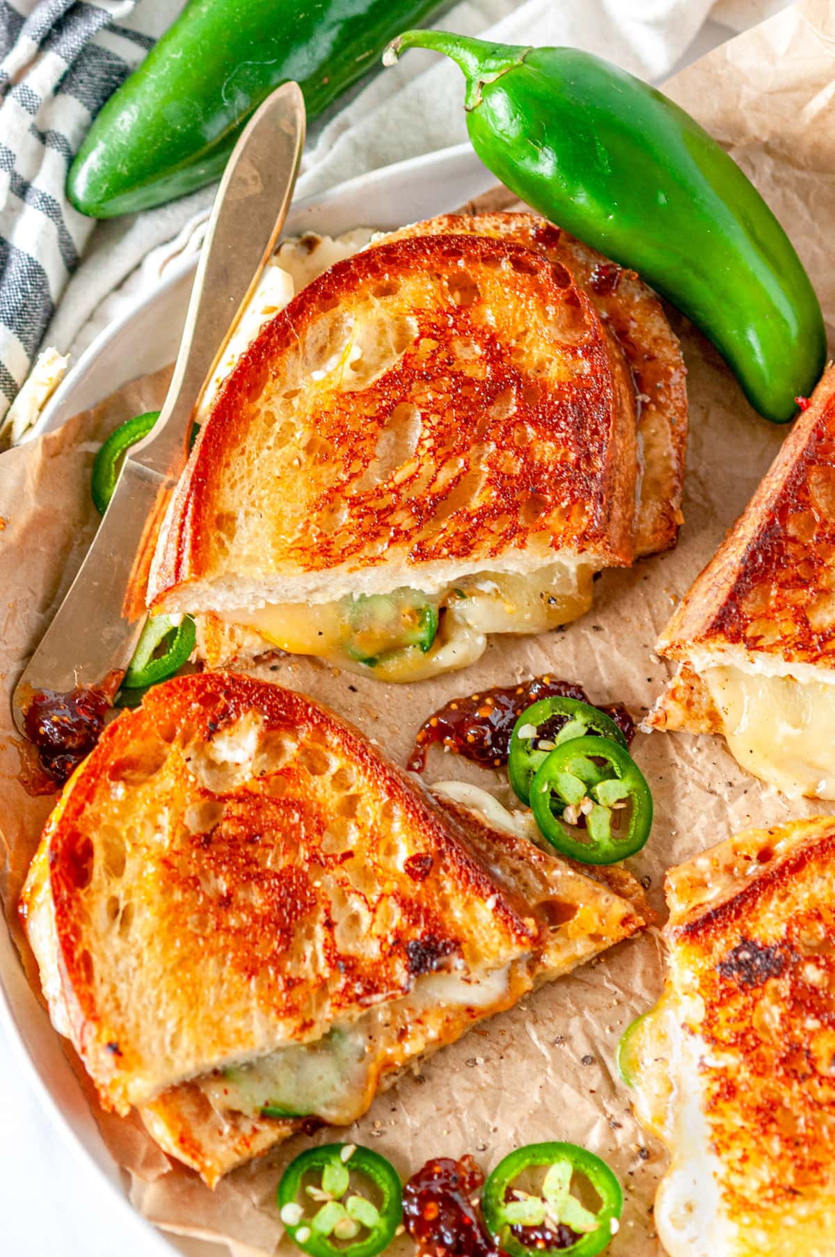 Spicy Grilled Cheese Sandwich sliced into halves with fresh jalapeno peppers on parchment paper