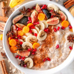 Banana Bread Overnight Oats in white bowl with sliced figs, golden berries, pomegranate seeds and star anise on white marble