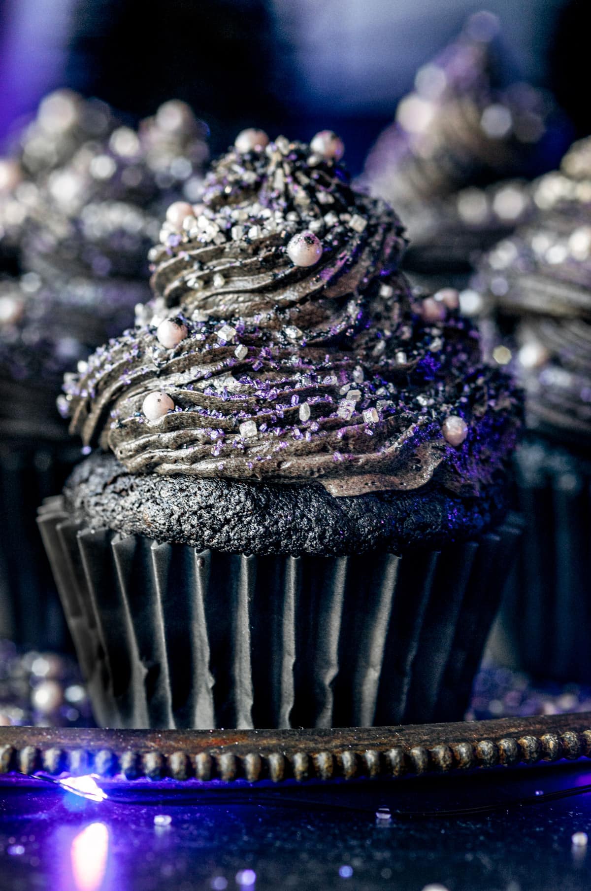 Black velvet cupcakes topped with sanding sugar and sprinkles on gray metal plate
