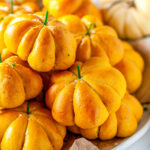 Pumpkin Bread Rolls with green chive stems piled on serving platter with pumpkins in background on white marble