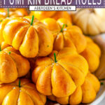 Pumpkin Bread Rolls with green chive stems piled on serving platter with pumpkins in background on white marble - purple rectangle with white text overlay