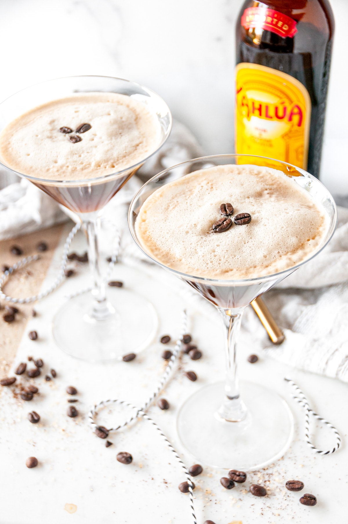 Espresso martini cocktail with foam and three coffee beans in glasses with kahlua bottle in the background