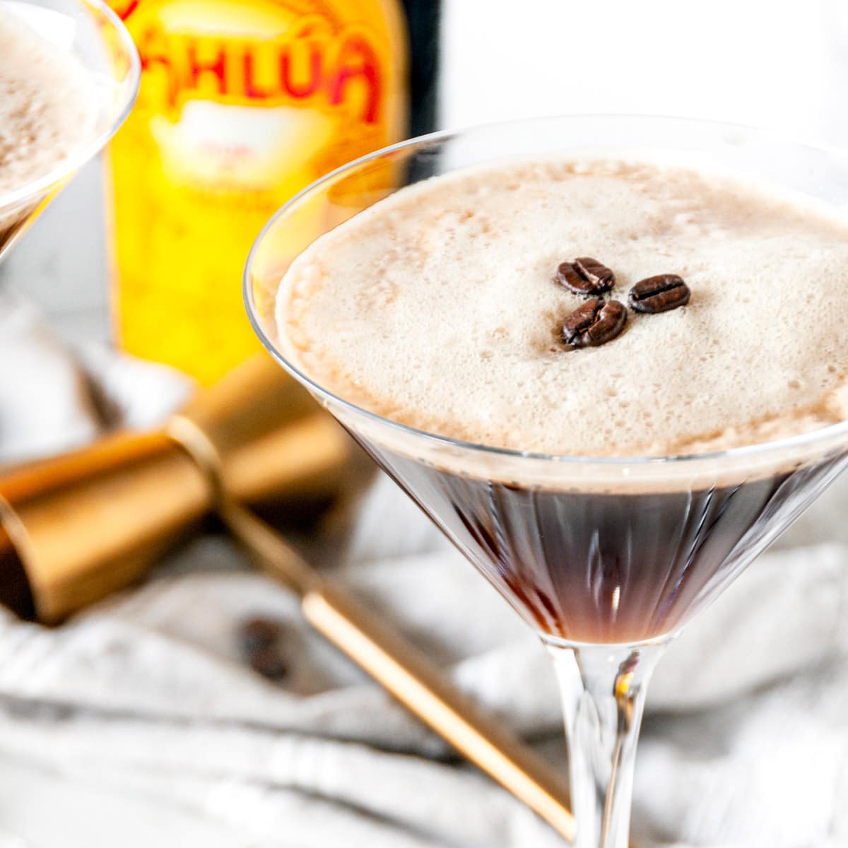 Espresso martini cocktail with foam and three coffee beans in glass close up with kahlua bottle in the background