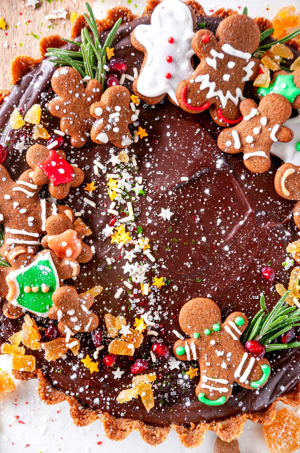Gingerbread Chocolate Tart topped with gingerbread cookies, festive sprinkles, and candied ginger on white marble