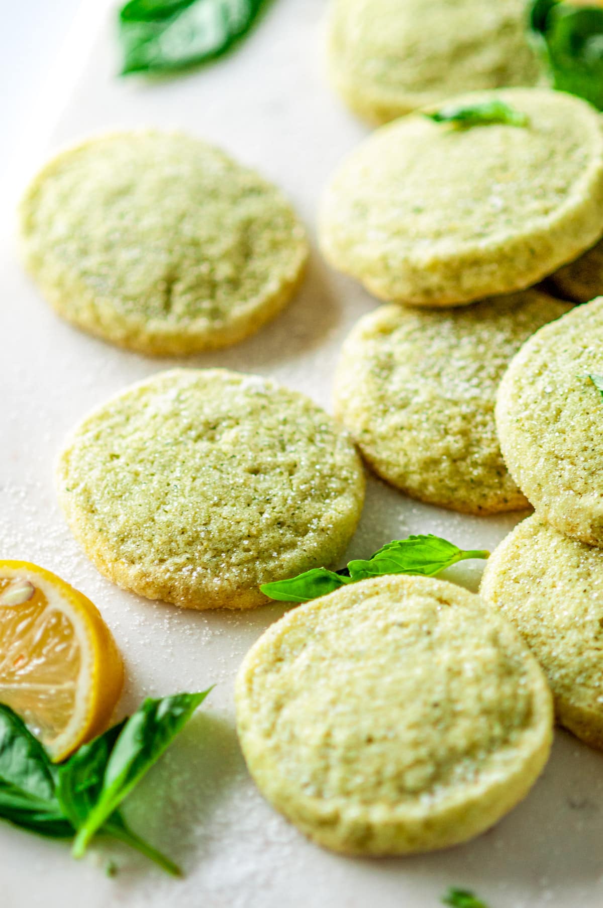 Lemon Basil Butter Cookies on white marble with sliced lemons and fresh basil leaves close side view