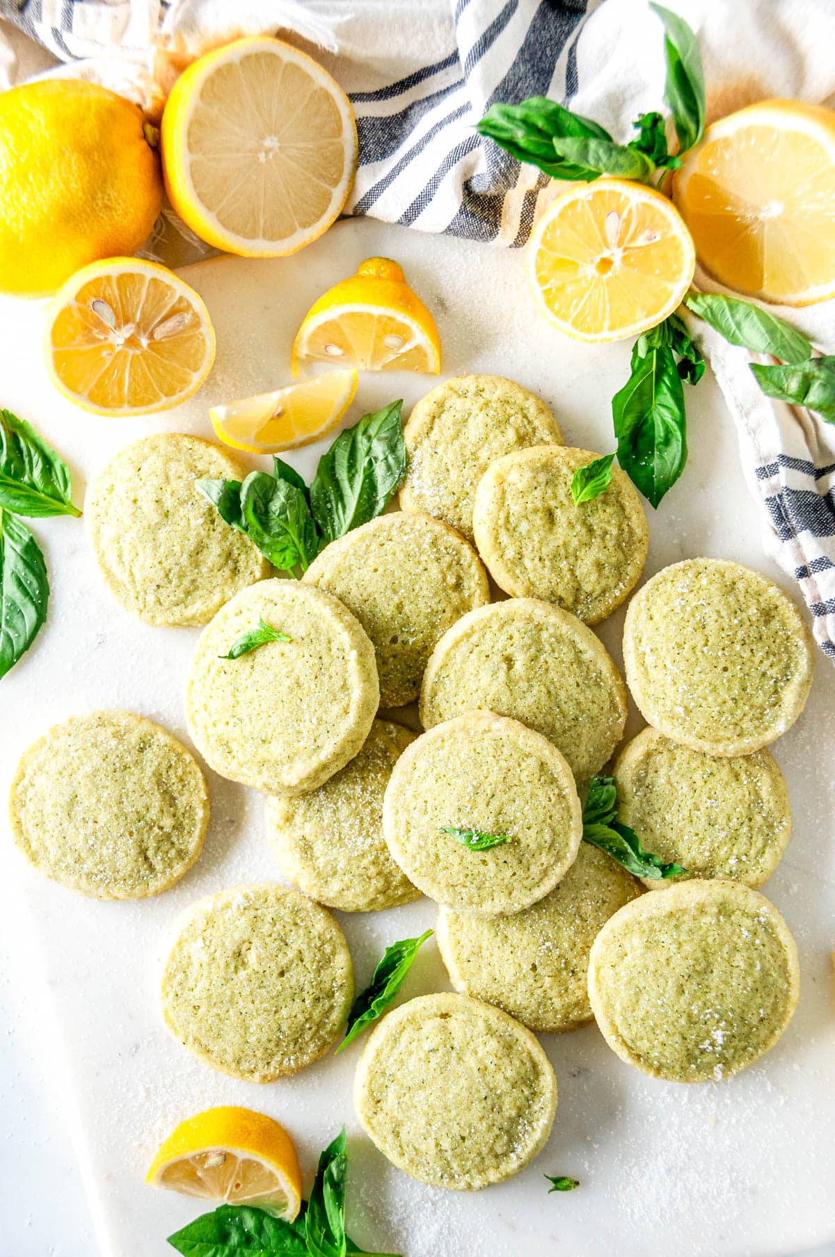 Lemon Basil Butter Cookies on white marble with sliced lemons and fresh basil leaves overhead view