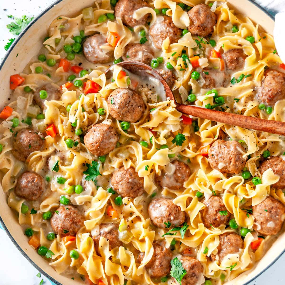 One Pot Swedish Meatball Pasta in blue le creuset braiser with wooden spoon on white marble overhead view