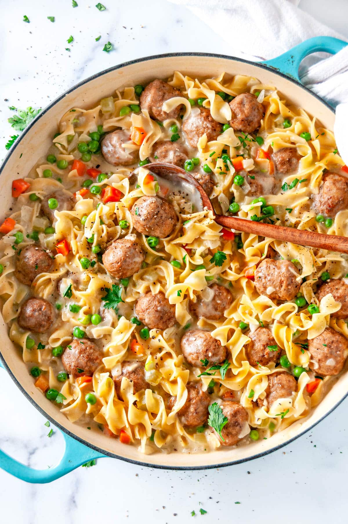 One Pot Swedish Meatball Pasta in blue le creuset braiser with wooden spoon on white marble overhead view