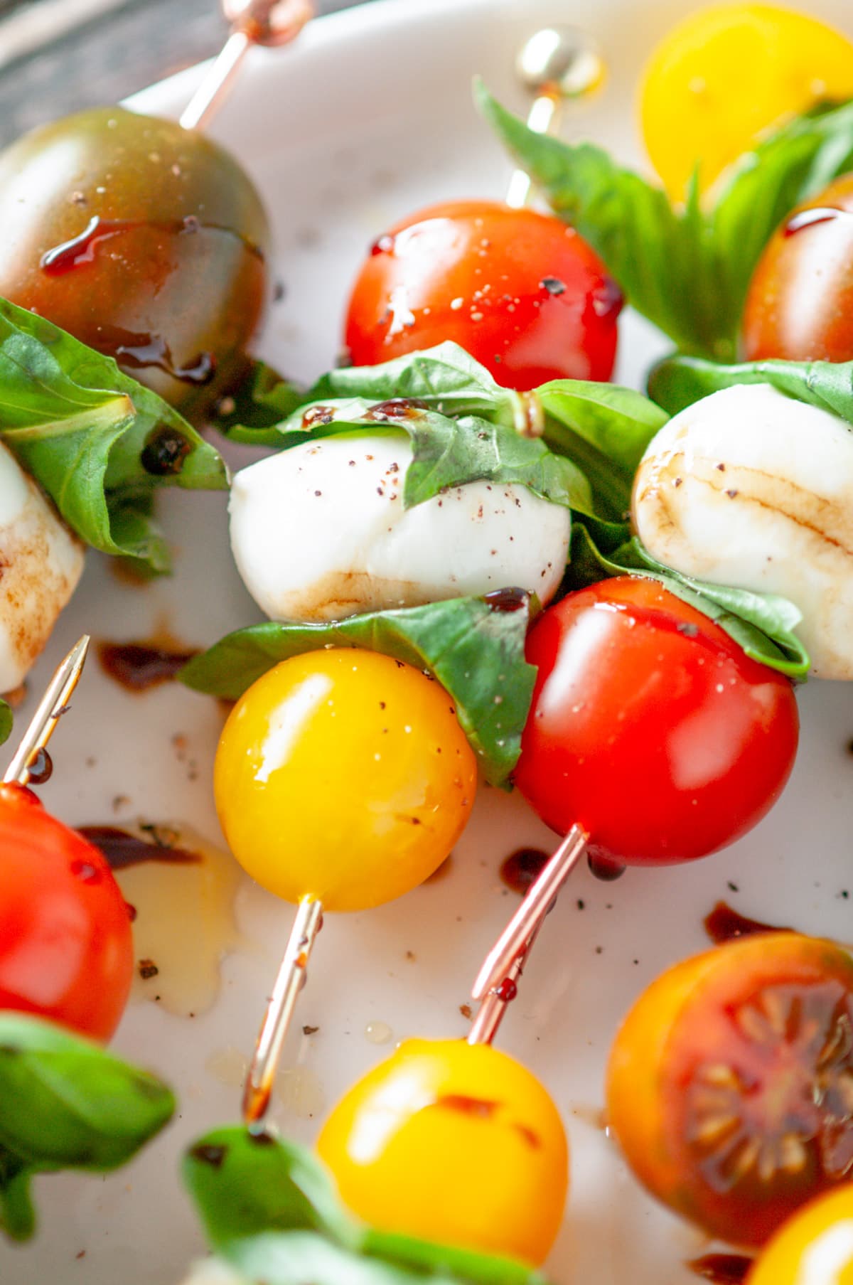 Caprese Salad Bites with heirloom cherry tomatoes, mozzarella balls, and fresh basil skewers on white plate