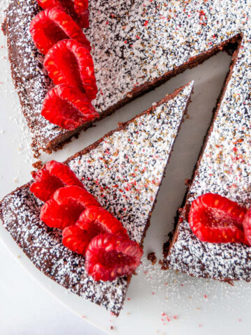 Chocolate Raspberry Flourless Cake sprinkled with powdered sugar on white cake stand with one slice cut overhead view