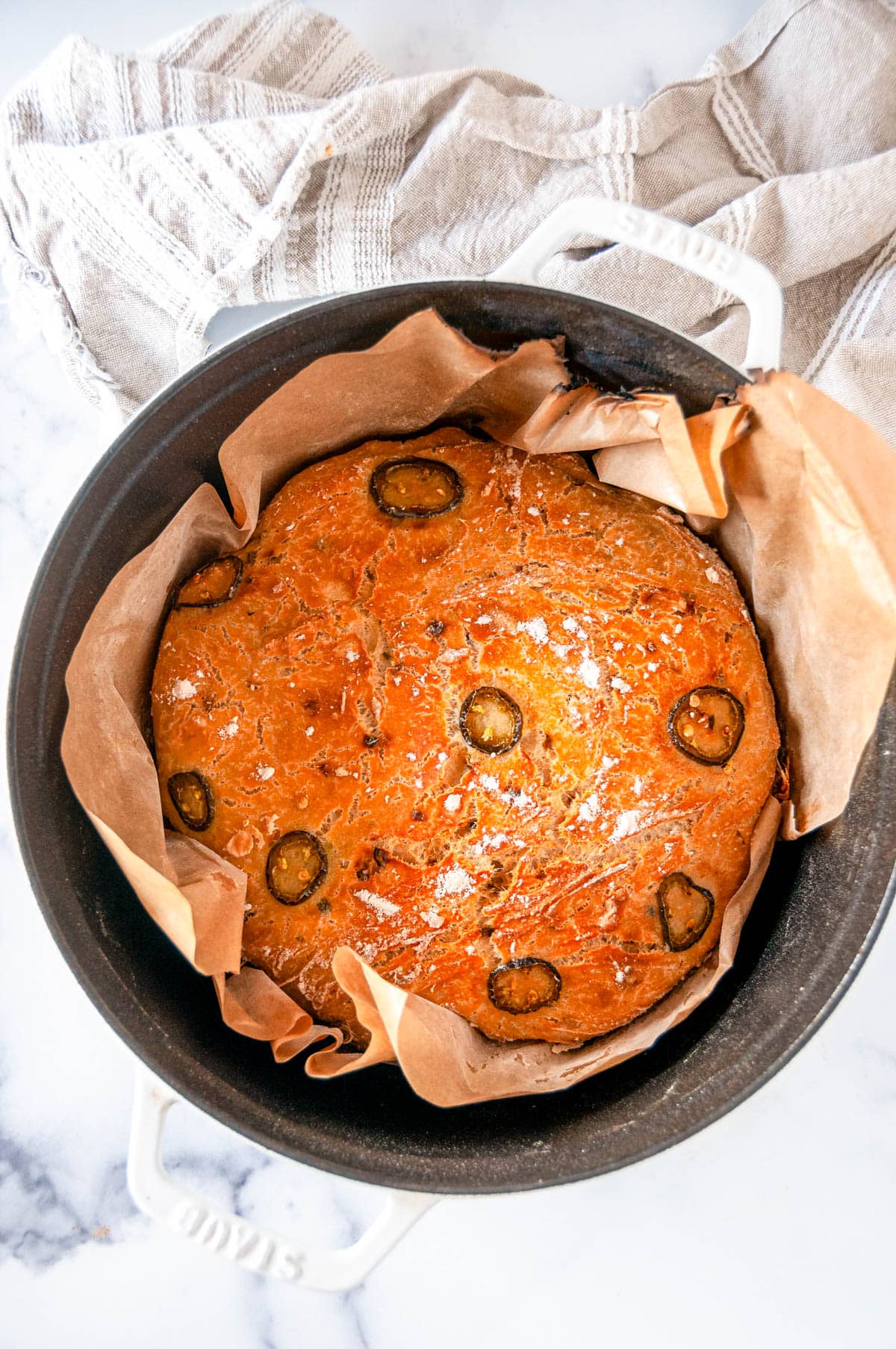 No Knead Jalapeño Cheddar Bread baked in white staub dutch oven with brown parchment paper overhead view