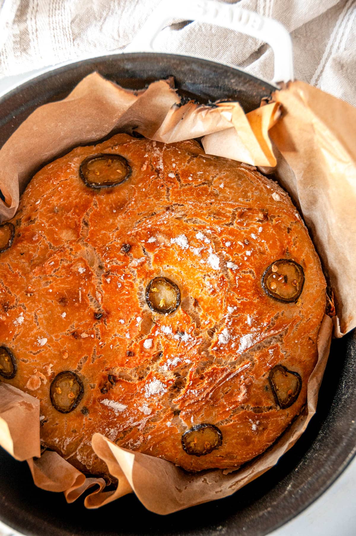 No Knead Jalapeño Cheddar Bread baked in white staub dutch oven with brown parchment paper overhead view close up