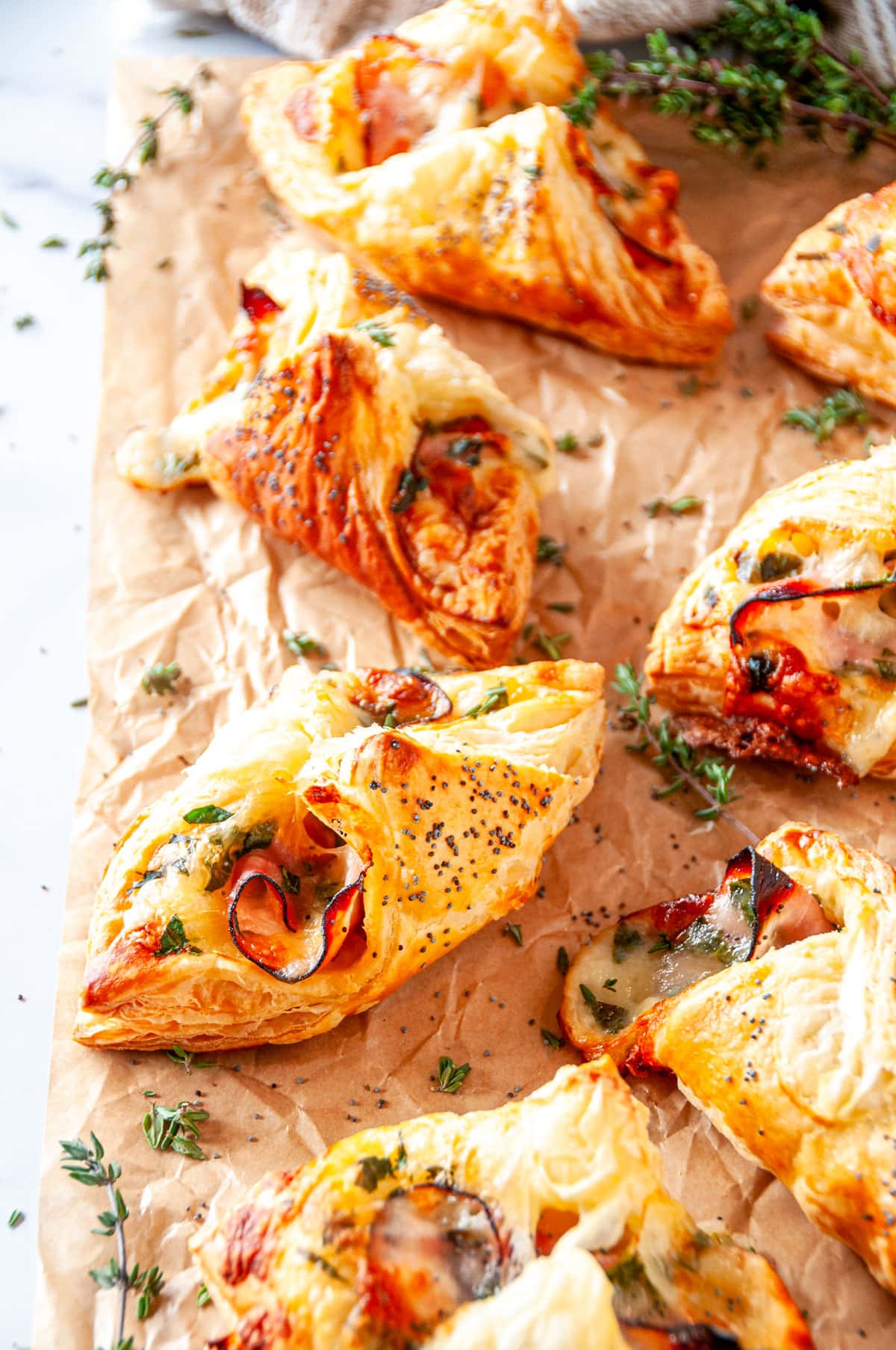 Cheesy Ham Spinach Puff Pastries on parchment paper and white marble with fresh thyme leaves