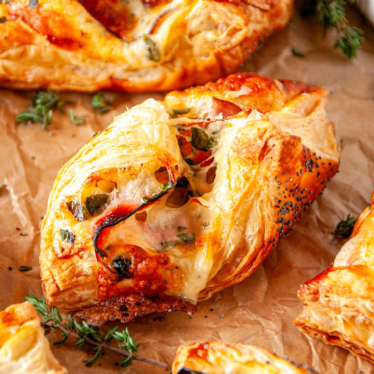 Cheesy Ham Spinach Puff Pastries on parchment paper with fresh thyme leaves close up