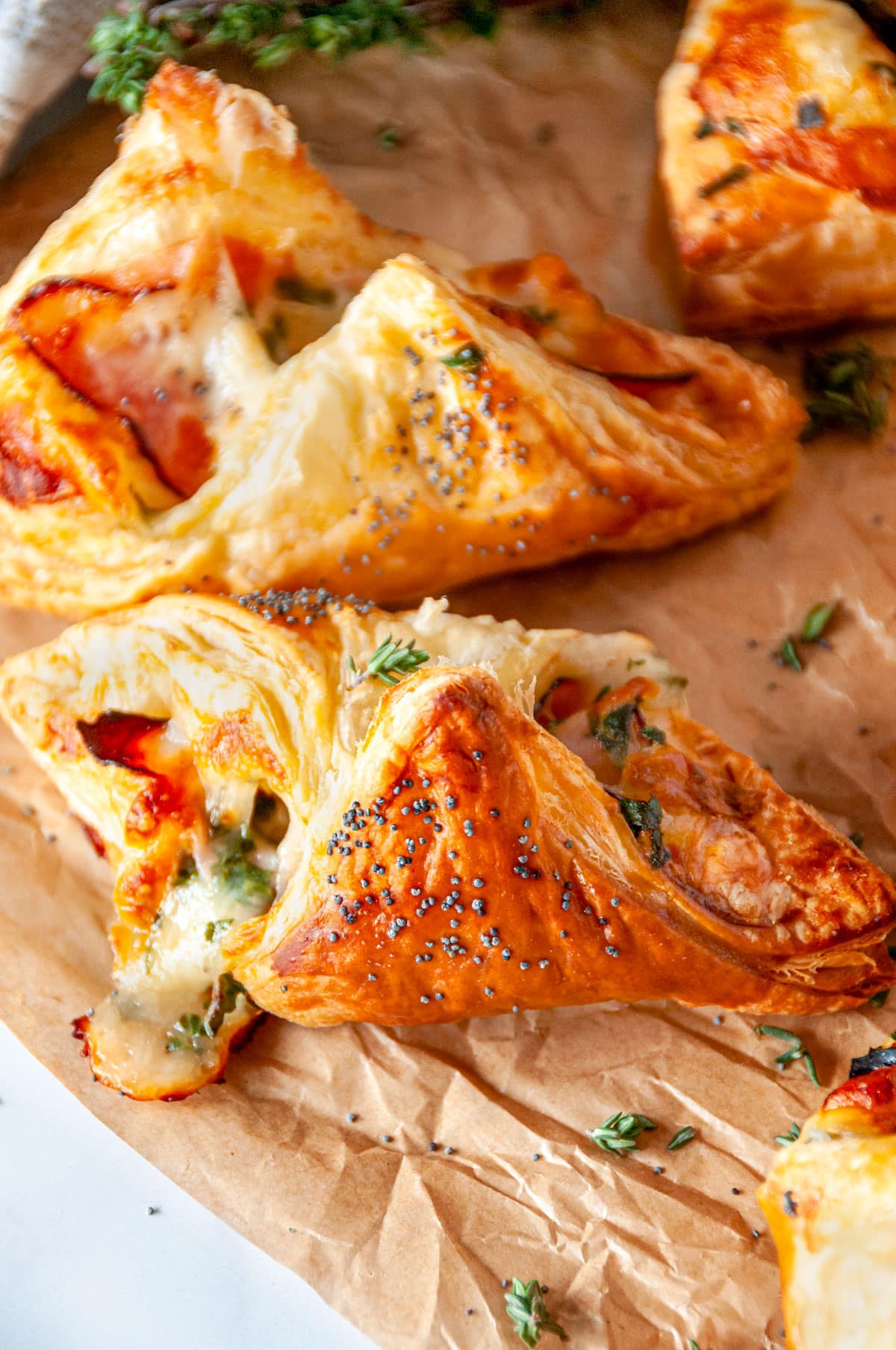 Cheesy Ham Spinach Puff Pastries on parchment paper with fresh thyme leaves close up