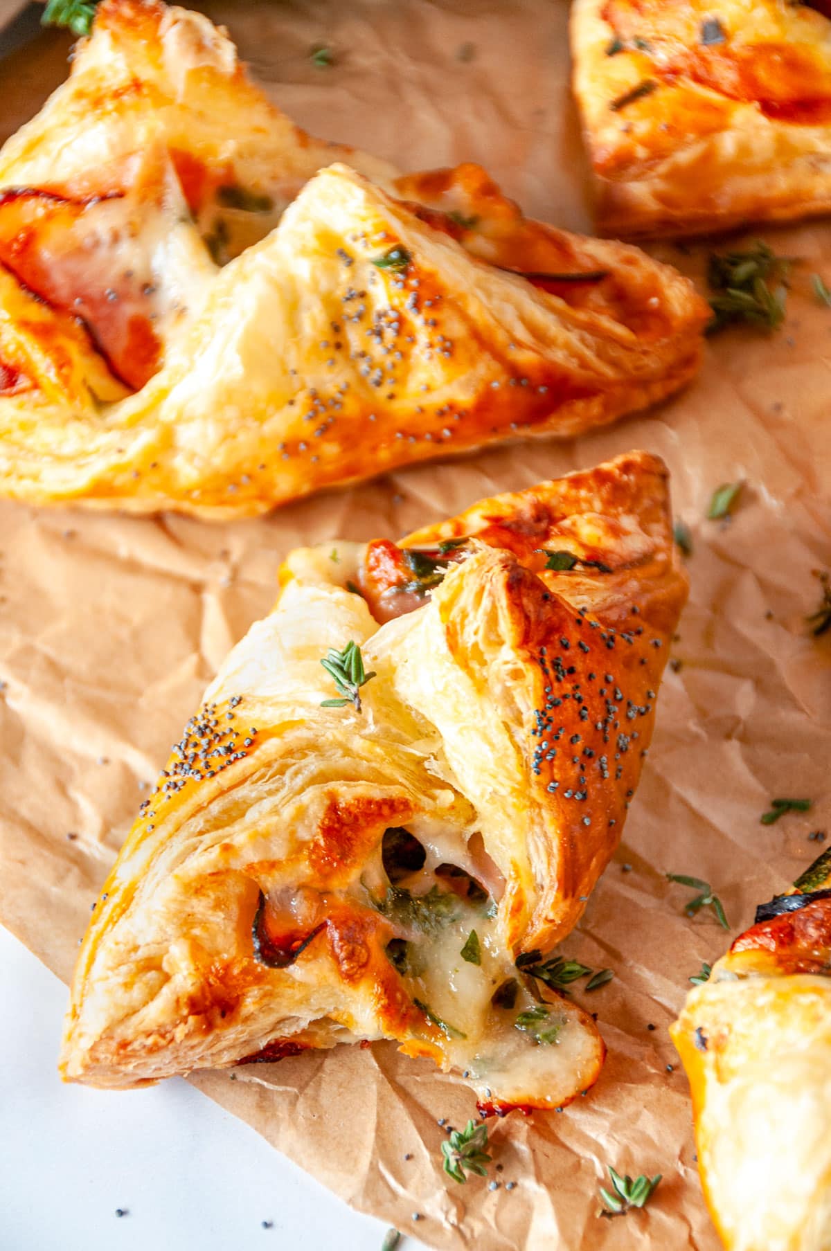 Cheesy Ham Spinach Puff Pastries on parchment paper and white marble with fresh thyme leaves close up