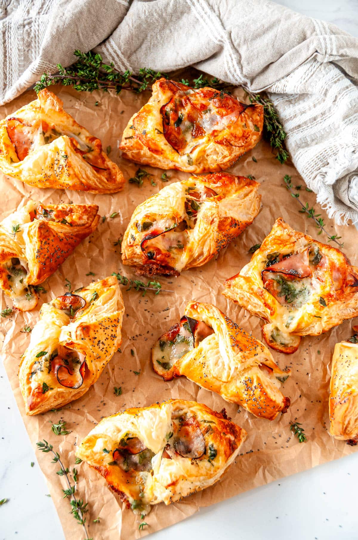 Cheesy Ham Spinach Puff Pastries on parchment paper and white marble with fresh thyme leaves overhead view