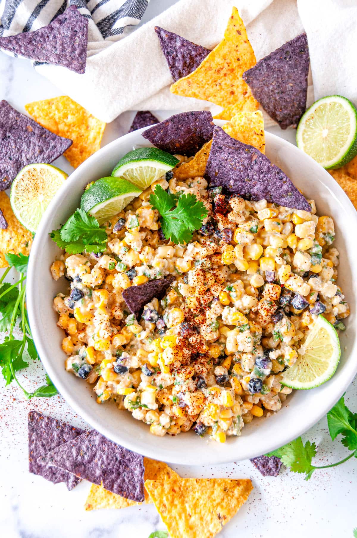 Elote dip in white bowl with purple and yellow tortilla chips overhead view
