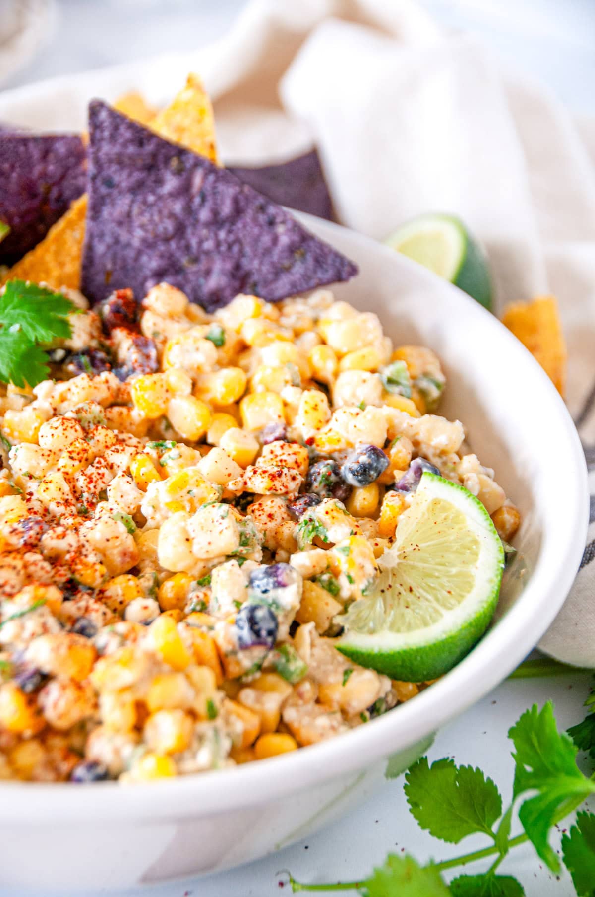 Elote dip in white bowl with purple and yellow tortilla chips side view close up