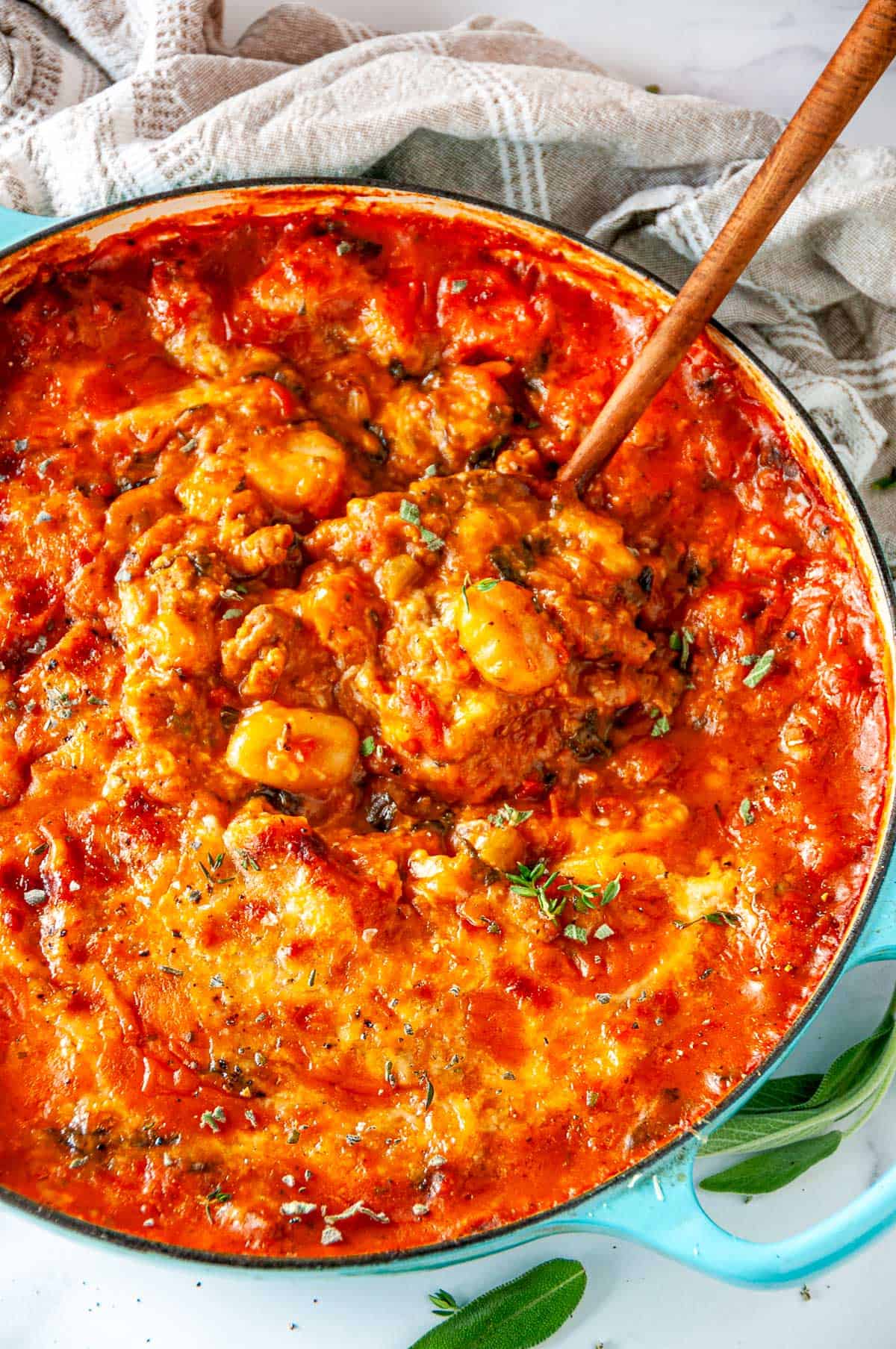 Dutch oven filled with one pot autumn gnocchi, with a wooden spoon scooping up the cheesy gnocchi, sausage, and squash.