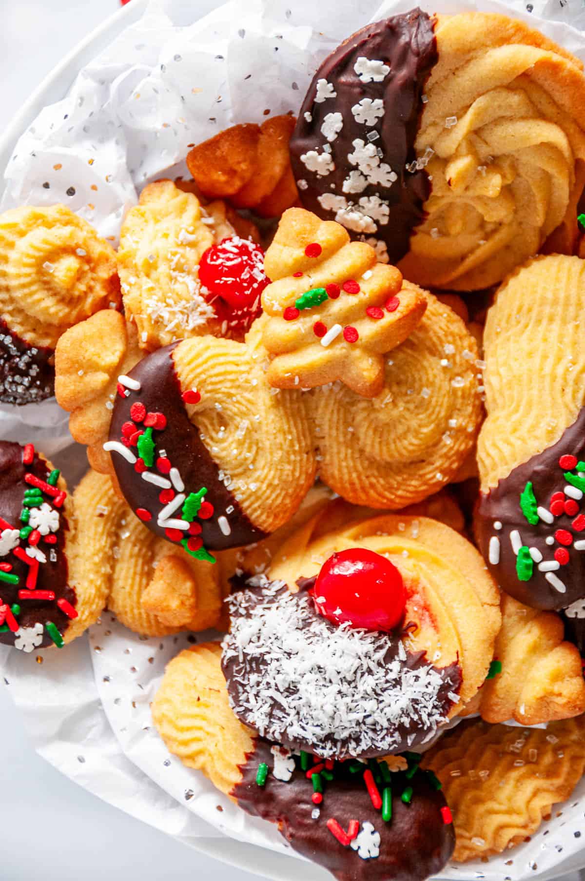 Italian Butter Cookies displayed in a white bowl with holiday sprinkles, chocolate dips, and Christmas ornaments