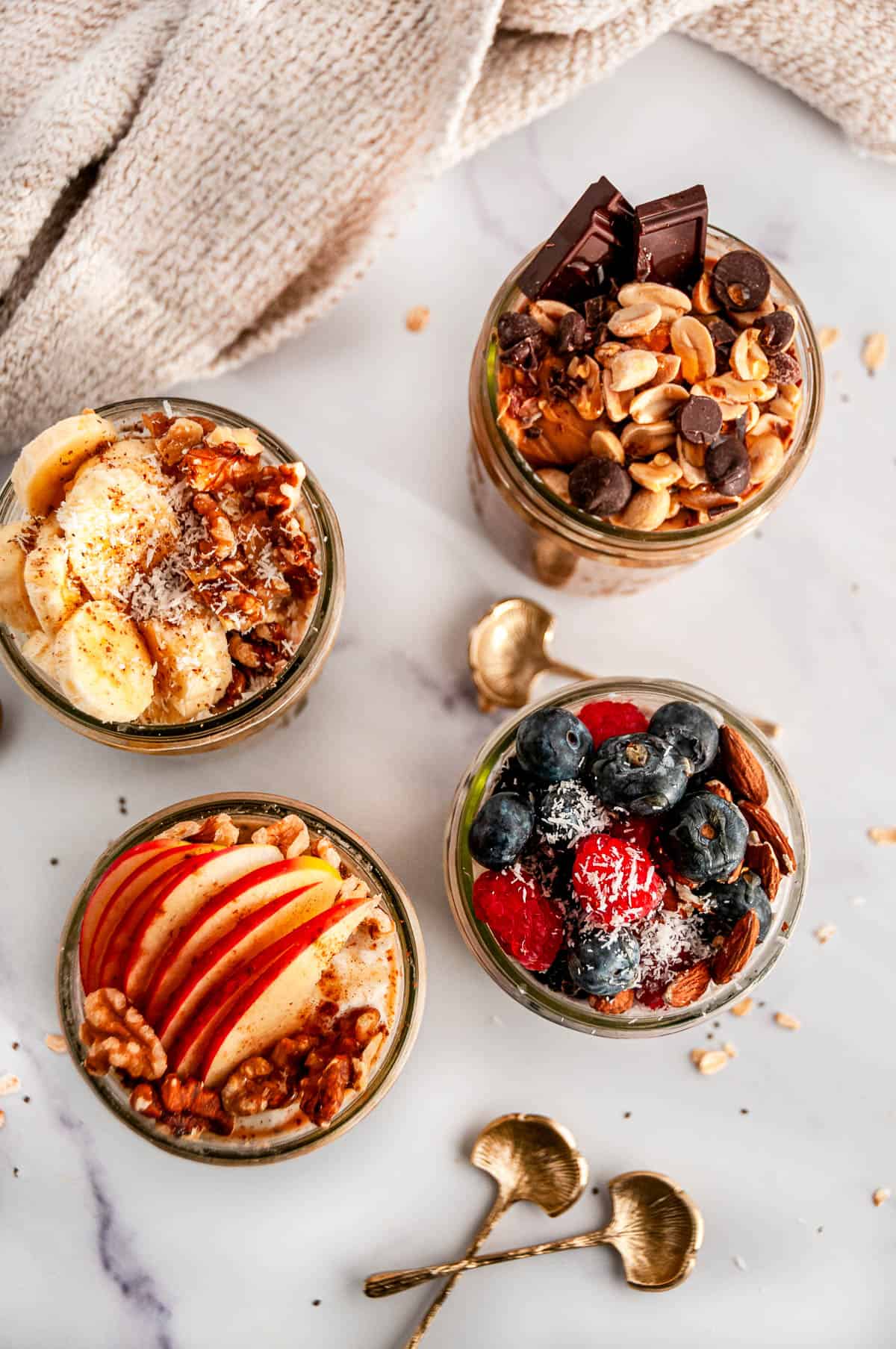 Four flavors of easy overnight oats in jars on a white marble surface