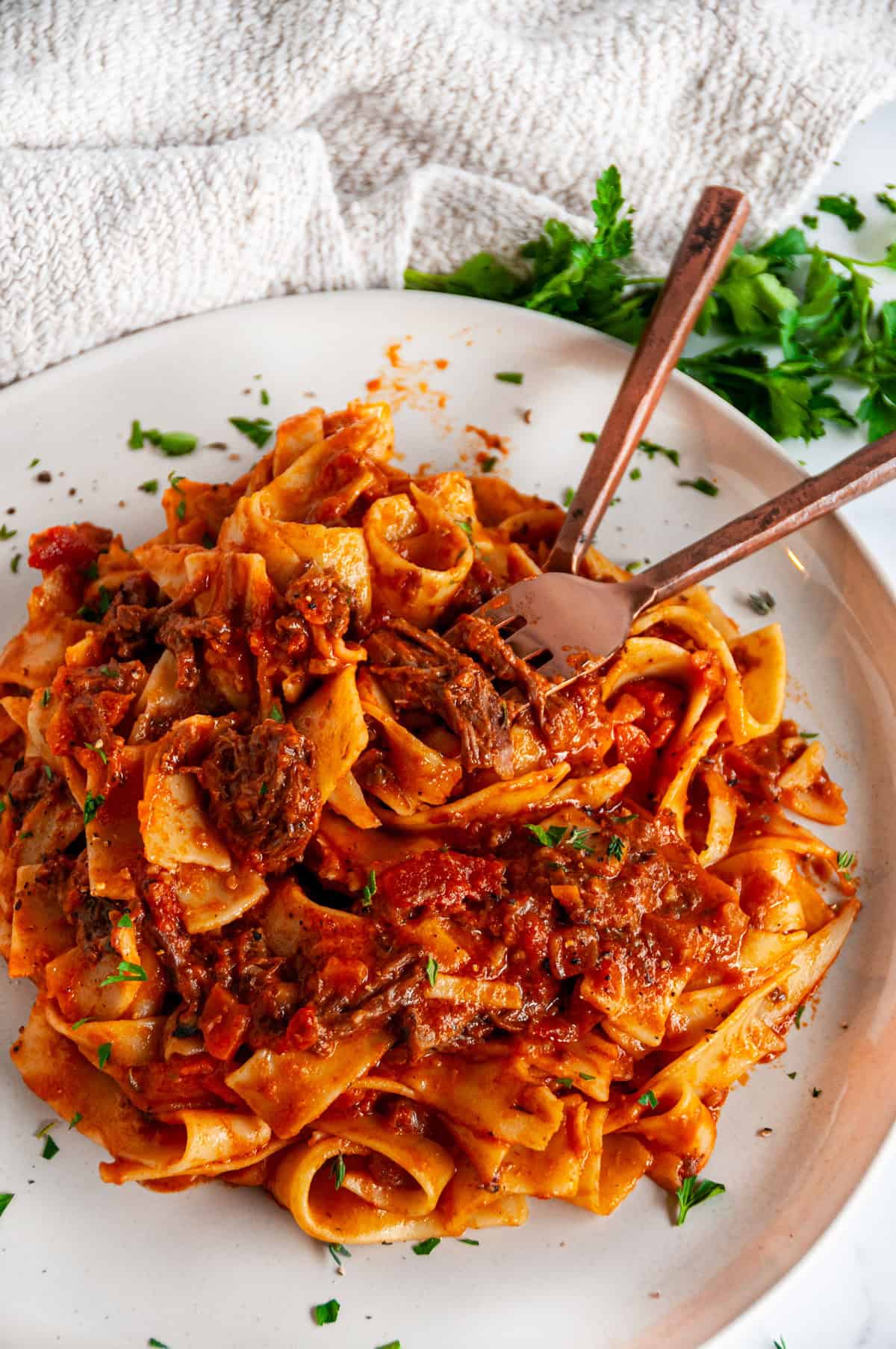 Instant Pot Beef Short Rib Pasta Ragu with tender shredded short ribs and wide pappardelle noodles in rich tomato sauce with fork and spoon in pasta, angled overhead.