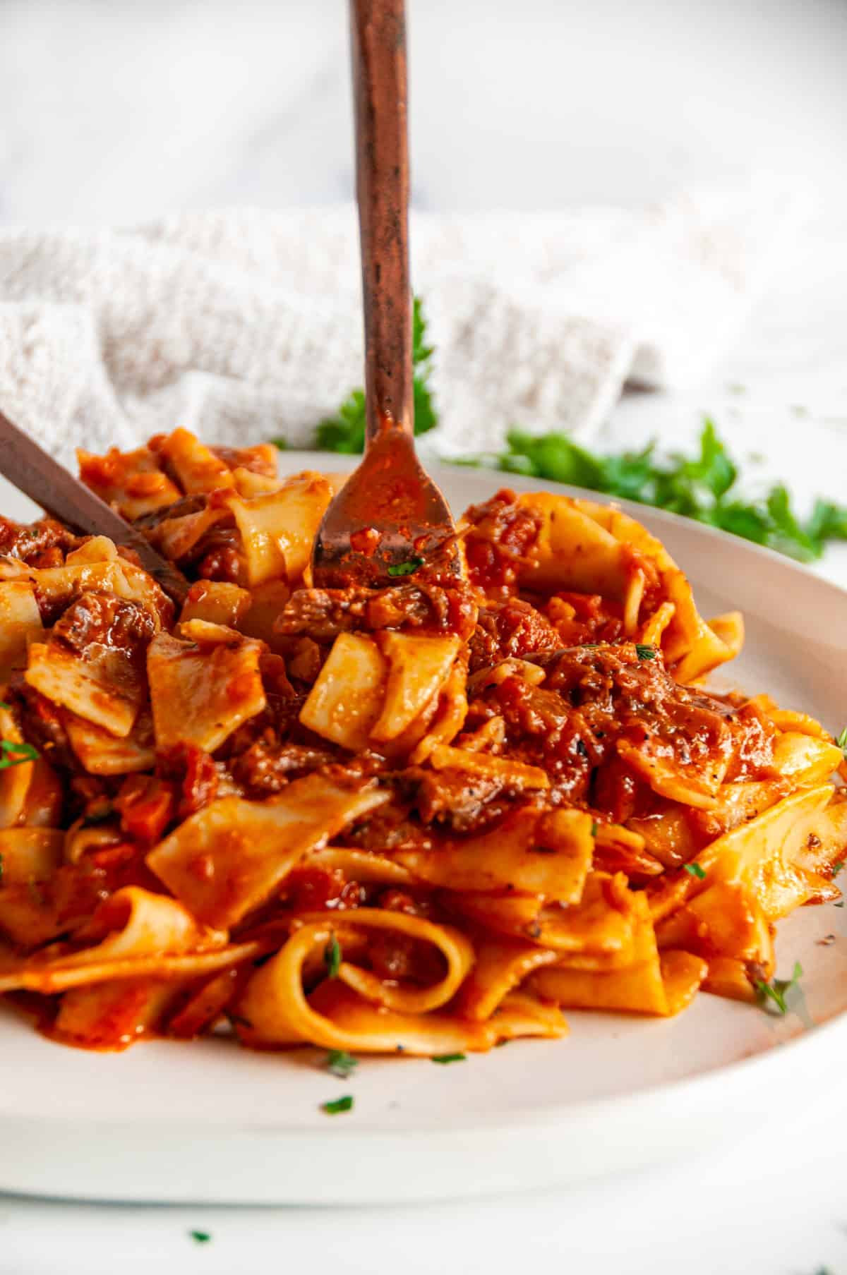 Instant Pot Beef Short Rib Pasta Ragu with fork lifting saucy pappardelle and braised beef in a red wine tomato sauce, side angle.